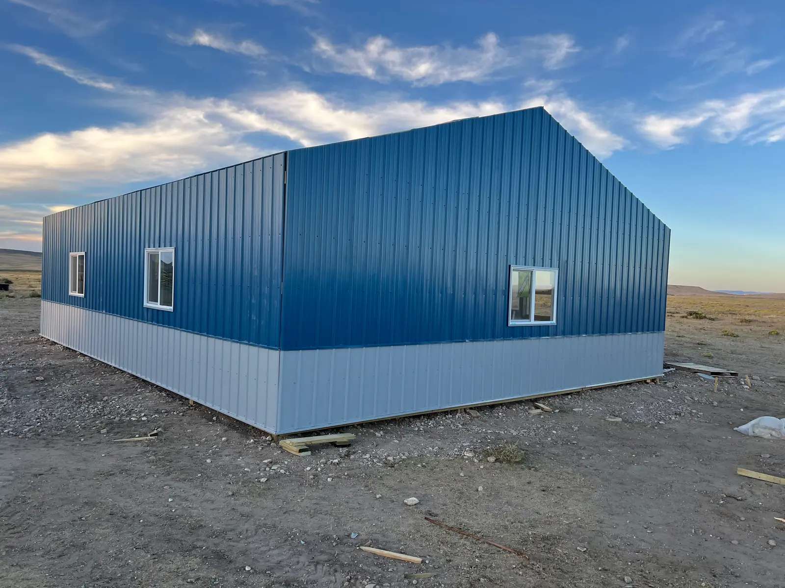 Blue metal outbuilding with light-gray lower panels and white-framed windows.