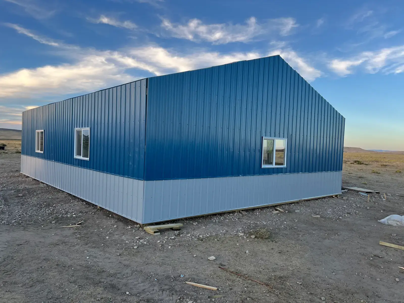 Blue metal-sided outbuilding with gray lower panels and white-framed windows.