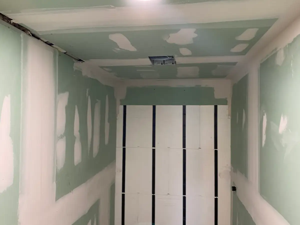 Narrow interior space with green wallboard, taped seams and a double doorway at the end.