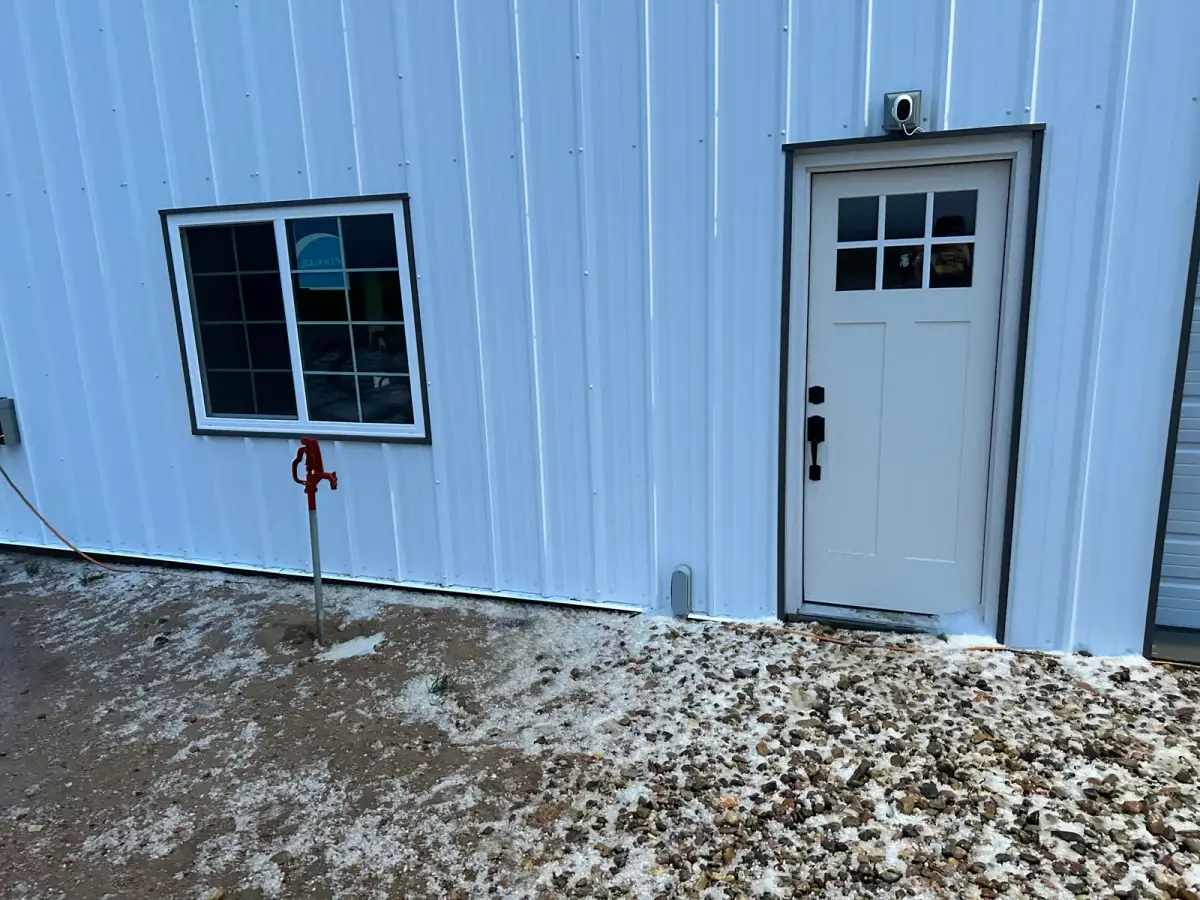 White entry door and dark-trimmed window installed in white metal siding.