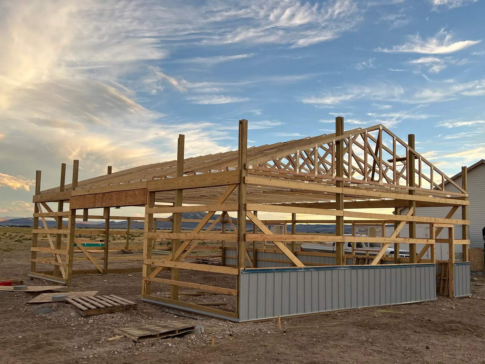 Roof trusses and timber framing on an Elite Level Construction post-frame building at sunset.