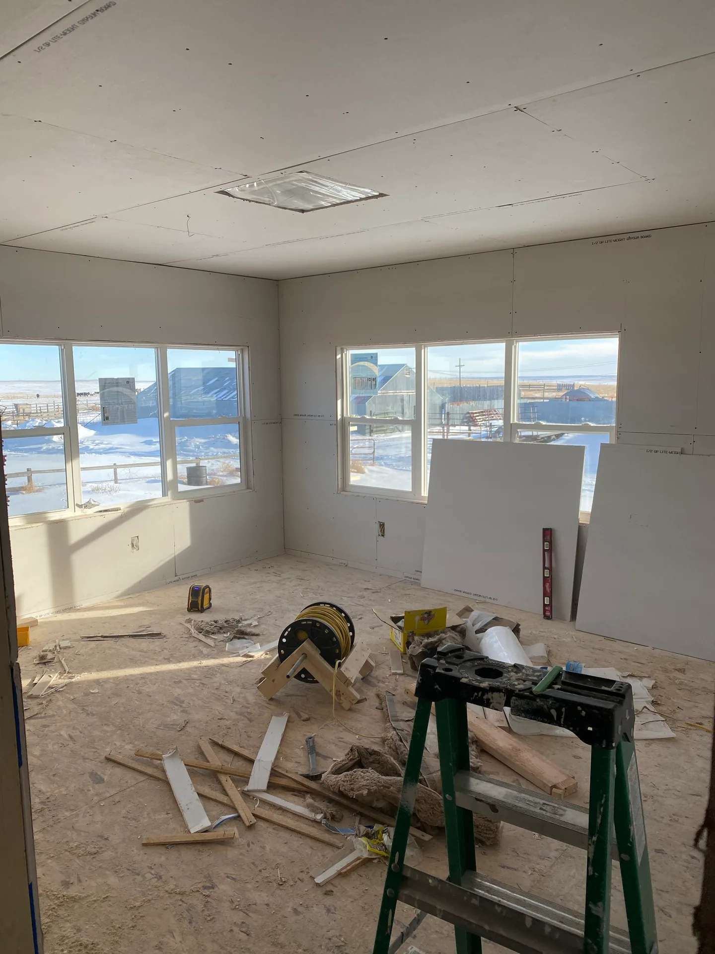 Drywall and window installation in progress inside a room with carpentry tools.