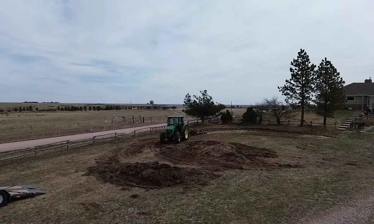 Elevated view of a tractor grading a building site beside an existing house and trees.