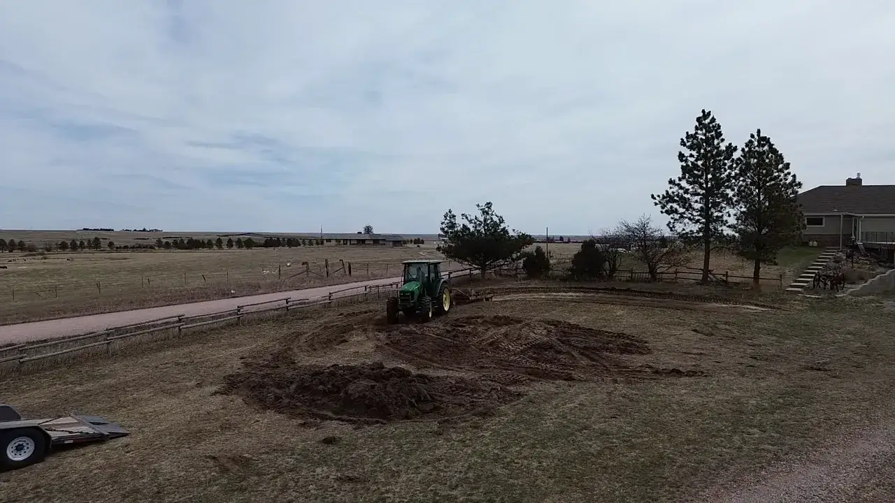 Elevated view of a tractor grading ground beside a house and pine trees.