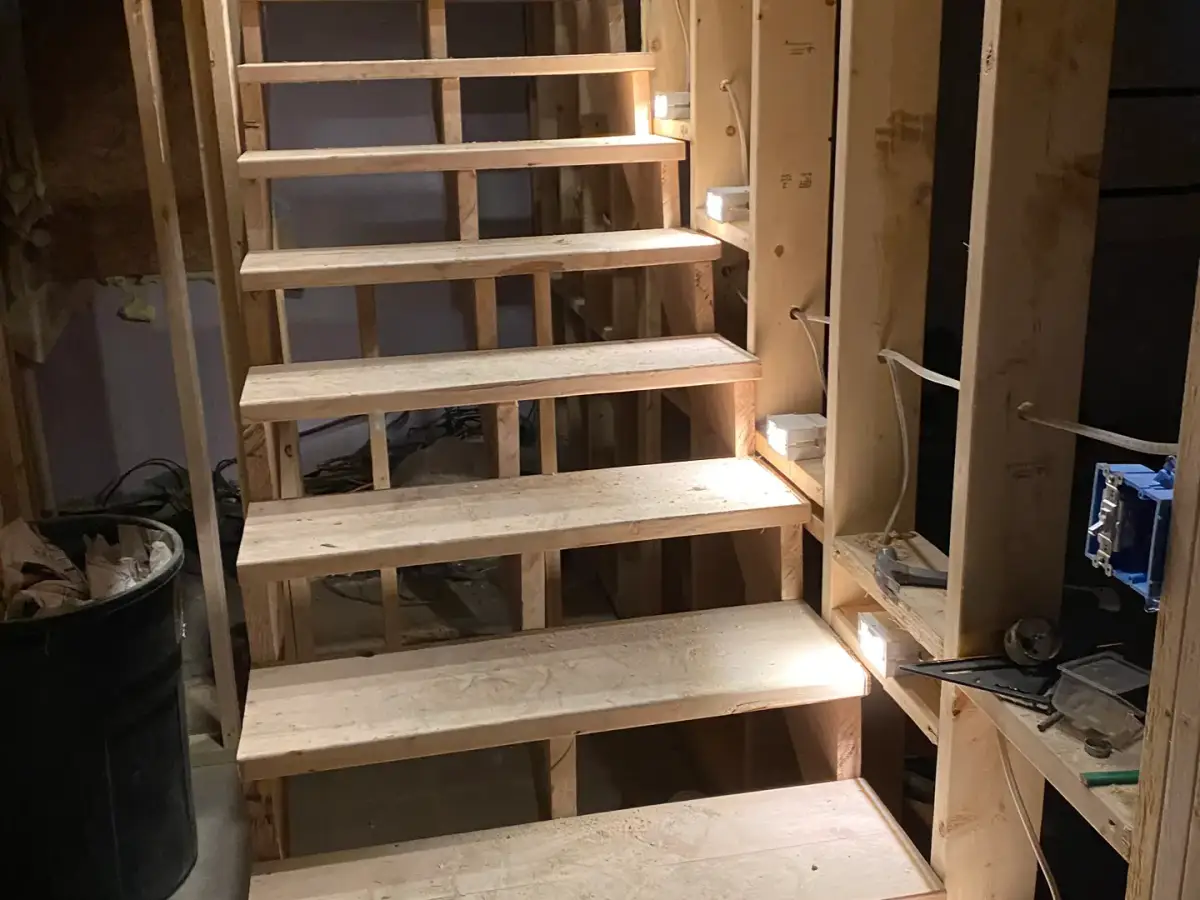 Unfinished wooden staircase between exposed wall studs, viewed from below.