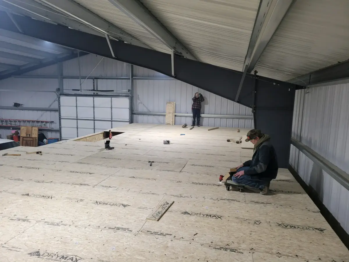 Crew laying subfloor panels on an upper level inside a steel-framed building.